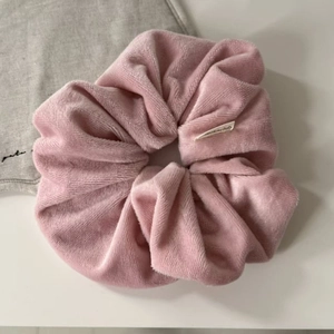Detailed close-up of soft pink velvet scrunchie featuring premium pleated texture and woven label
