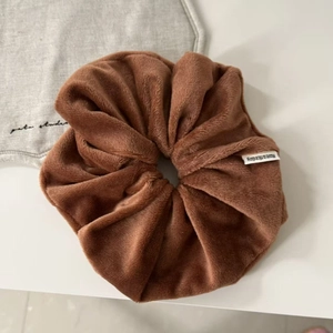 Close-up of a brown velvet scrunchie with a white woven label on a soft neutral surface