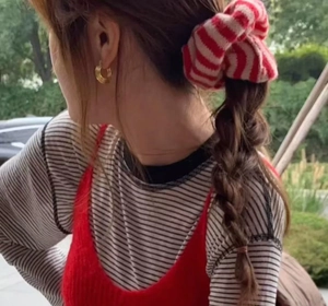 Detail of a red and white striped knit scrunchie worn on a braided hairstyle
