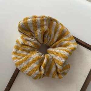 Detail shot of yellow and beige striped knit hair scrunchie on a wooden frame