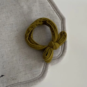 Detail of an olive green fabric scrunchie with a bow on a grey linen background