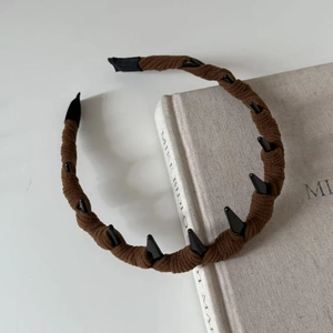 Dettaglio di cerchietto in maglia marrone con denti antiscivolo su un libro di lino