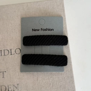Detail of two black twill fabric hair clips on a decorative paper display card