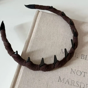 Dettaglio di un cerchietto in maglia marrone con borchie nere su un libro vintage