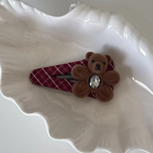 Détail de la pince à cheveux BB à carreaux rouges avec un ours floqué et un strass brillant