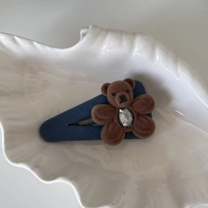 Détail d'un ours floqué marron avec cristal coeur sur pince en tissu bleu ciel