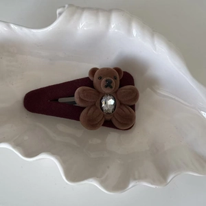 Détail d'une barrette ours en velours marron avec strass sur un support bordeaux