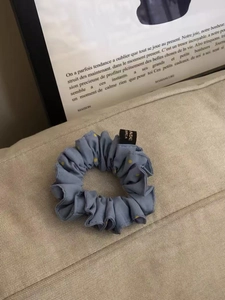 Detail eines blauen Satin-Haargummis mit Punkten auf einem beigen strukturierten Sofa