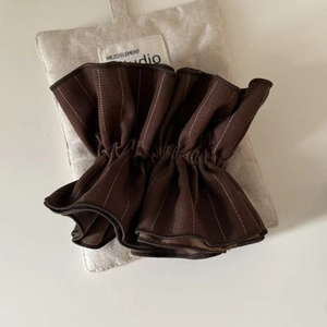 Close-up of dark brown striped fabric scrunchie with pleated texture on linen pouch