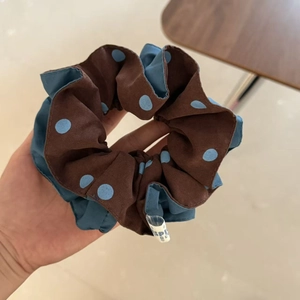 Detail of coffee brown polka dot hair scrunchie with soft fabric texture and side label
