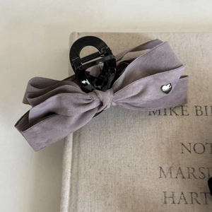 Détail d'une pince à cheveux avec nœud en tissu gris et boucle en forme de cœur argenté