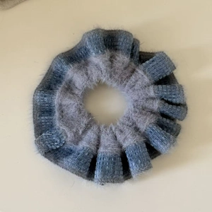Macro detail of knit fabric scrunchie with grey faux fur trim and contrast blue color