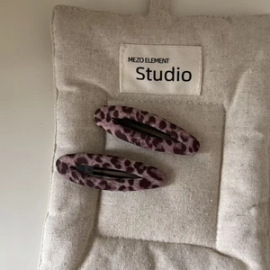 Close-up of two pink leopard print hair clips on a textured beige linen background