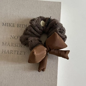 Détail d'un chouchou en maille marron foncé avec nœud en soie et bouton blanc sur livre