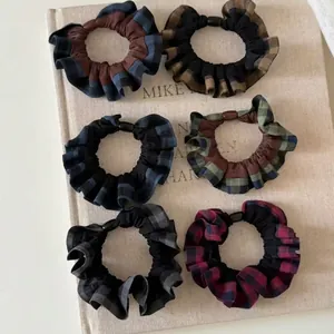 Set of six college style plaid scrunchies with pleated fabric texture on beige linen