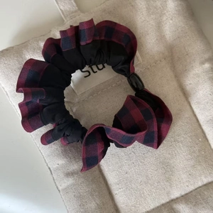 Macro detail of red and black plaid scrunchie with adjustable buckle on canvas background