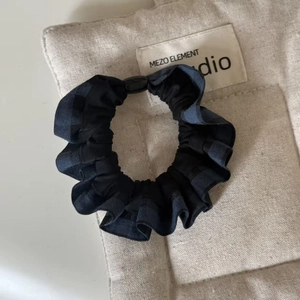 Detail of navy plaid scrunchie with ruffled fabric texture and black decorative button