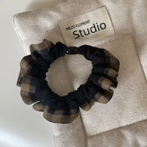 Detail view of plaid and black fabric scrunchie with decorative bead on canvas background