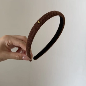 Detail shot of a dark brown knitted headband featuring a small golden heart metal buckle