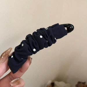 Détail d'une pince à cheveux banane bleu marine à pois avec texture de tissu plissé
