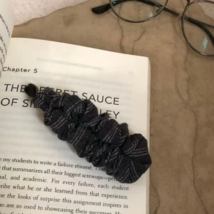 Gros plan d'un chouchou à rayures gris foncé posé sur un livre ouvert avec lunettes