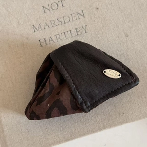 Detail of triangular leather coin purse with leopard print accent and silver logo plaque