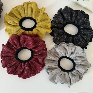 Detail view of four textured knitted scrunchies in mustard, black, wine, and grey