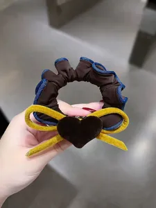 Dettaglio macro dello scrunchie con fiocco di velluto bordo denim e ciondolo a cuore