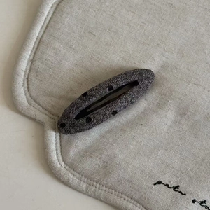 Detail shot of a grey wool BB hair clip with black polka dots on a linen surface