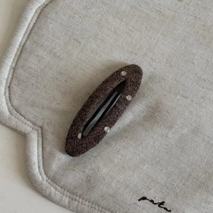 Detail view of a brown polka dot fabric wool hair clip on a textured linen background