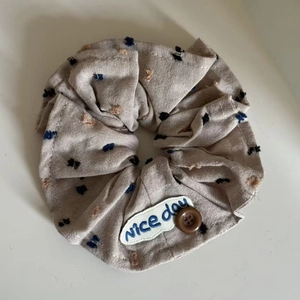 Detail of oatmeal fabric scrunchie with embroidered polka dots and button decorative accent