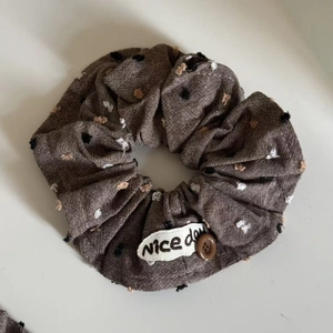 Detail of coffee brown pleated hair scrunchie with embroidery and button ornament