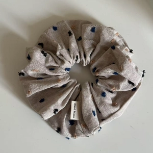 Detail of oatmeal-colored hair scrunchie with dot embroidery and Hand Made label