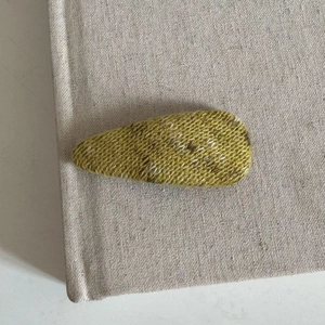 Knitted teardrop hair clip in yellow-green blend wool on a minimalist beige book background