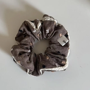 Detail of coffee brown fabric scrunchie with lace edges and colorful embroidered dots
