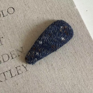 Close-up detail of dark blue knitted tweed fabric texture on a teardrop BB hair clip