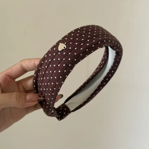 Detail of knitted wide headband in dark brown with white polka dots and golden heart charm