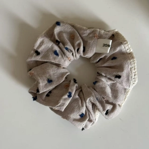 Detail of oatmeal fabric scrunchie with colorful heart pattern and white lace edging
