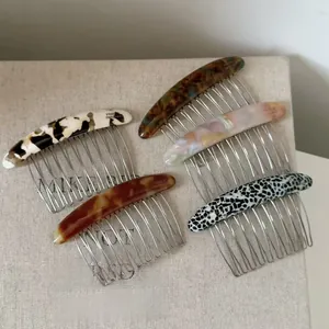 Detail view of five acetate hair combs with marble textures and sturdy metal teeth on fabric