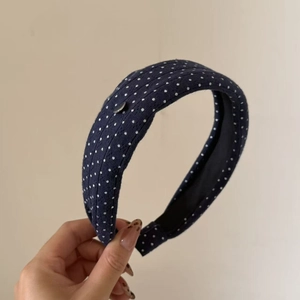 Detail of navy blue knitted headband with white polka dots and silver metal buckle
