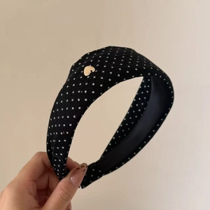 Detail of a wide knitted headband with polka dots and a golden heart metallic logo