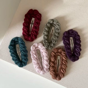 Set of six handmade knitted hair clips in assorted colors on a soft canvas background