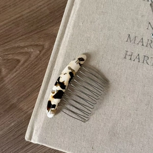 Close-up of tortoise shell acetate hair comb with metal teeth on a linen book