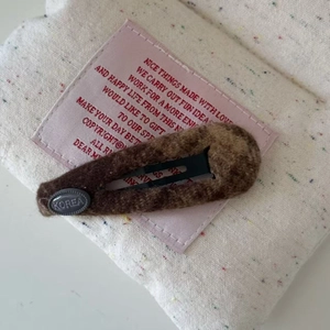 Dettaglio del fermaglio per capelli in peluche marrone con etichetta Korea su tessuto