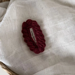 Deep red handmade knitted oval hair clip with wave edge on rustic white background