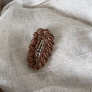 Detailed view of hand-knitted brown wool BB hair clip with woven texture on white linen
