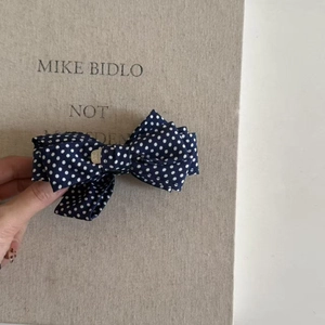 Detail of navy blue polka dot bow hair clip featuring a layered fabric design and gold accent