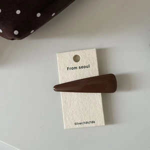 Close-up of minimalist dark brown glossy hair clip on a premium white card display