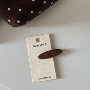 Detailed macro view of a glossy dark brown oval hair clip on a minimalist display card