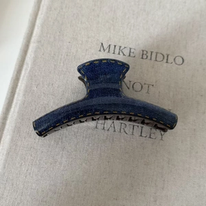 Detail of blue denim fabric hair claw clip with yellow contrast stitching on a book